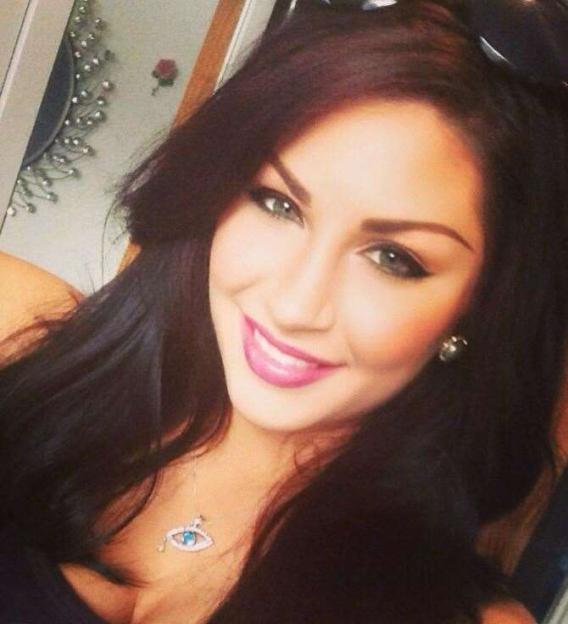 A smiling woman with dark hair wearing a necklace with an eye-shaped pendant.