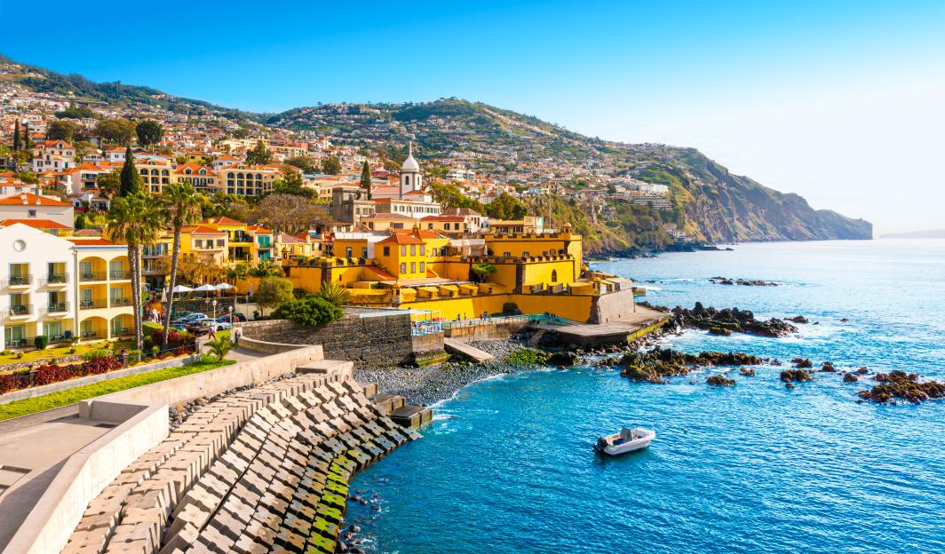 Panoramic view of Funchal, Madeira, with colorful buildings along the coast and a mountainous backdrop.