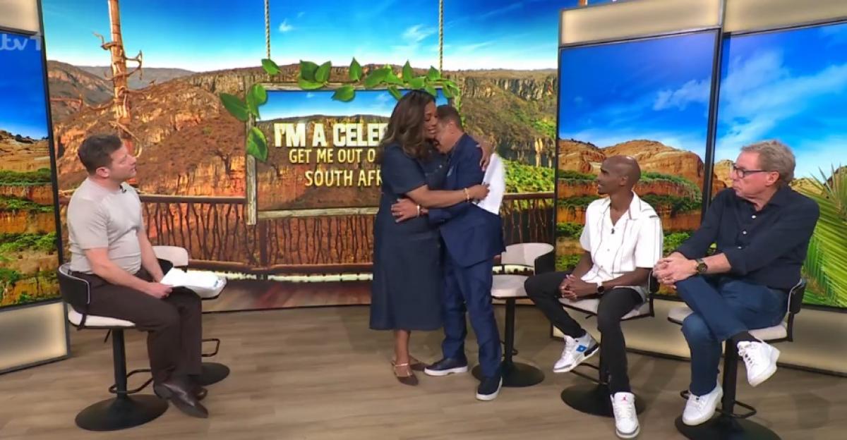 Four people on a talk show set with "I'm A Celebrity South Africa" signage, with two people embracing in the middle.