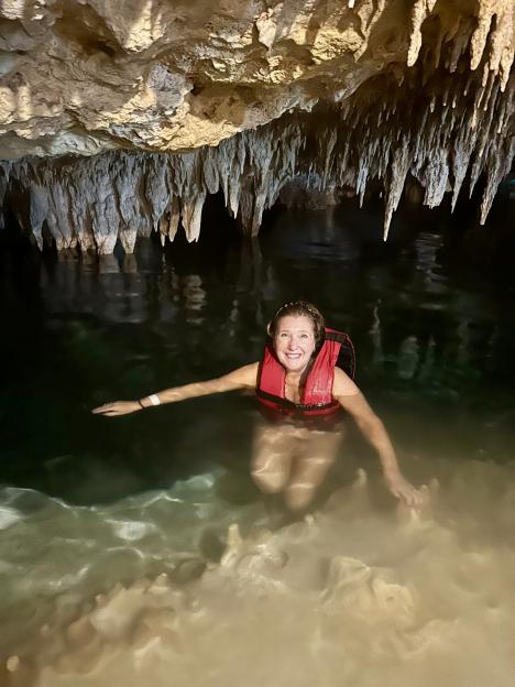 Lisa Minot smiling while swimming in a cenote with a red life vest.