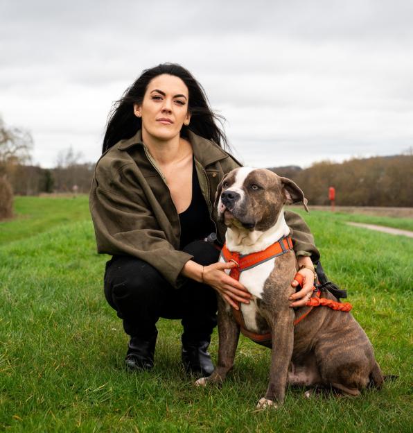 Fiona Mulkerrins-Dixon, a woman who was defrauded, crouches next to her dog in a grassy field.