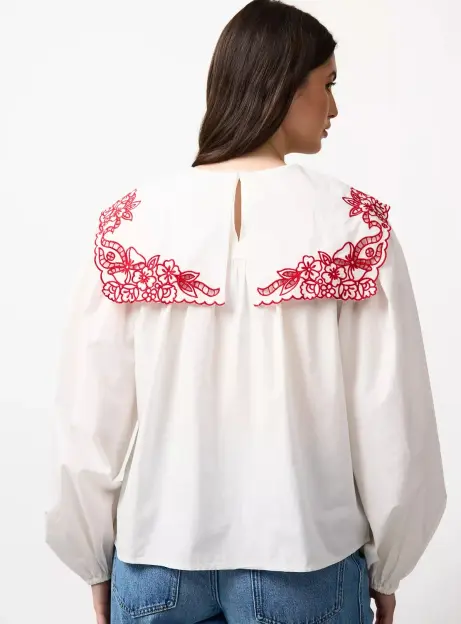 Back view of a white blouse with a large red floral embroidered collar worn by a model.