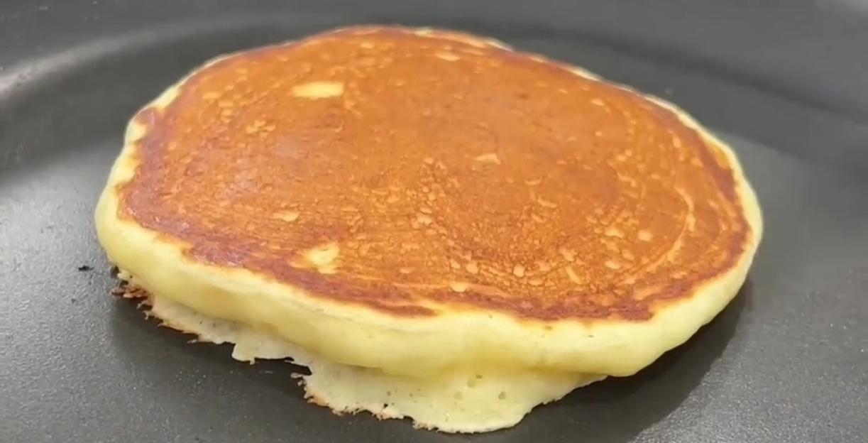 A pancake cooking in a black frying pan.