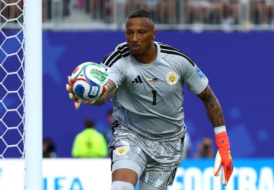 A soccer goalie in a gray uniform and orange gloves catches the ball.
