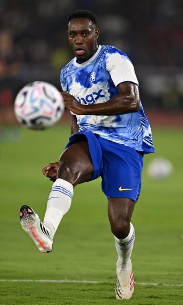A Chelsea FC player in a blue and white tie-dye jersey runs after a soccer ball.