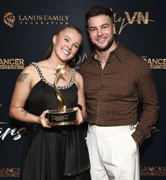 JoJo Siwa holding a Star Humanitarian Award trophy next to Chris Hughes at the Dancers Against Cancers Gala of the Stars.