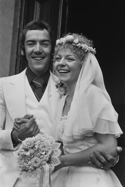 Black and white photo of Robert Lindsay in a white suit embracing his bride Cheryl Hall who is holding a bouquet.