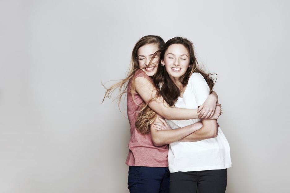 Studio portrait of two women hugging each other, eyes closed, and smiling.
