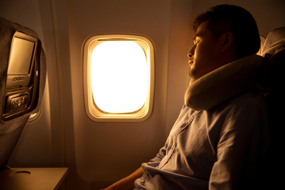 A young man with closed eyes sleeping comfortably in an airplane seat next to a window.