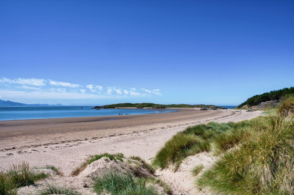 Newborough Beach in North Wales with sand dunes and clear blue water.