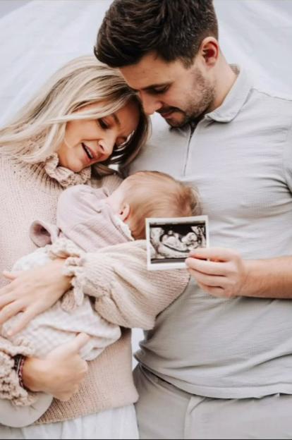 A woman holding a baby, and a man holding up an ultrasound picture.