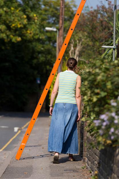 A woman walking under an orange ladder, risking bad luck, in Twickenham, Greater London, UK.