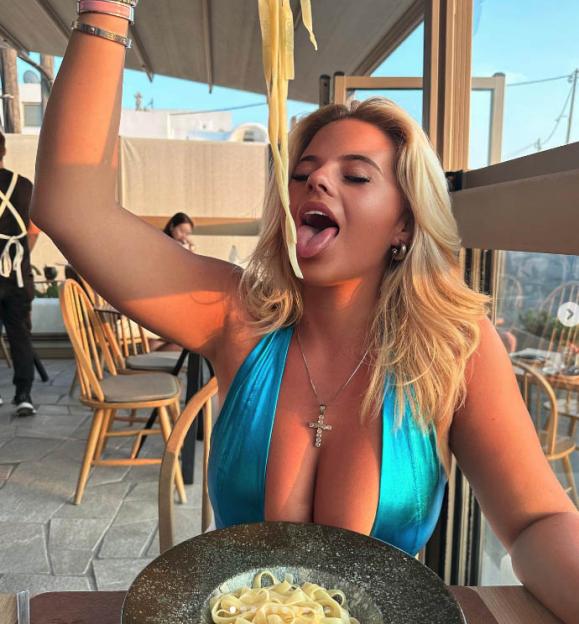 a woman in a blue bikini is eating noodles with her tongue out