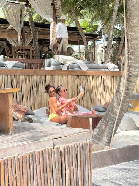 Two women relaxing at a beach bar, one taking a selfie.