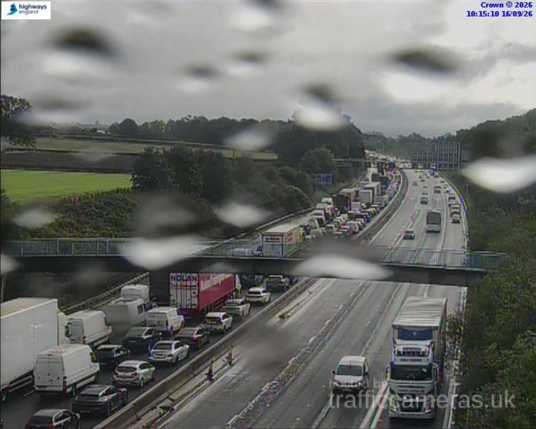 A traffic camera view of a busy motorway with heavy traffic, including a long line of stationary vehicles.