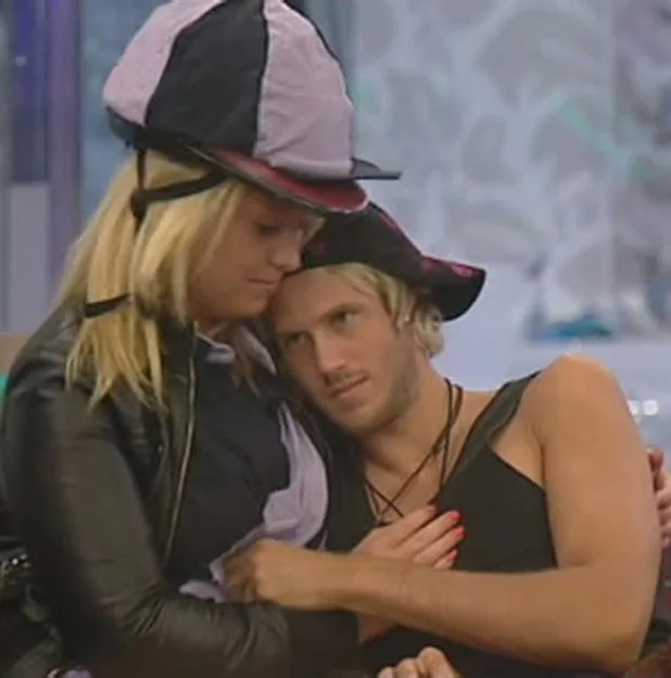 A blonde woman wearing a riding helmet hugs a man wearing a black cap.