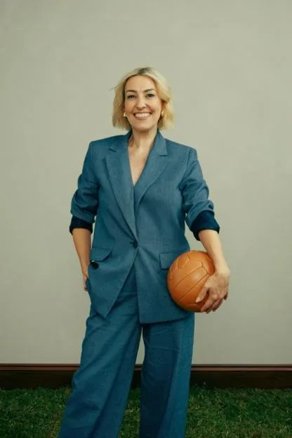 Portrait of a blonde woman wearing a blue suit and holding a vintage leather football.
