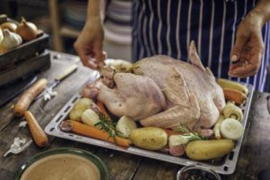 Hands preparing a raw turkey with vegetables on a roasting pan.