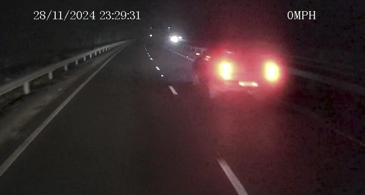 Matthew Newton in a blue plaid suit, light blue checkered tie, sunglasses, and holding a drink with a strawberry.