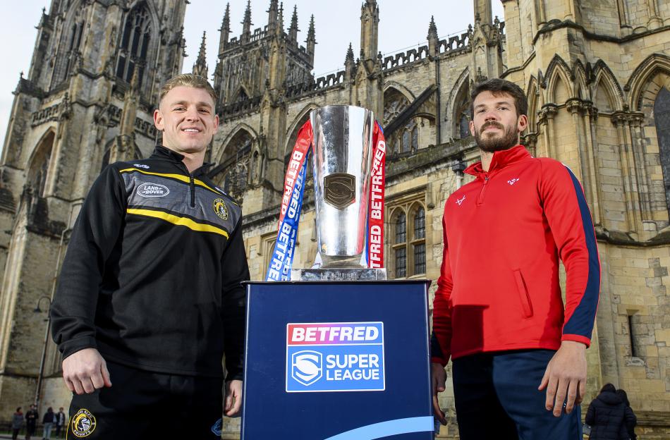 Liam Harris (left) and another rugby player stand on either side of the Betfred Super League trophy, in front of a Gothic building.