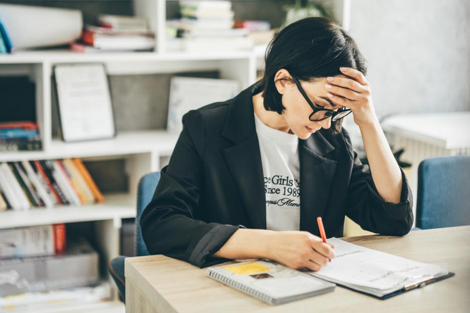 A teacher with a headache working at her desk in a classroom.