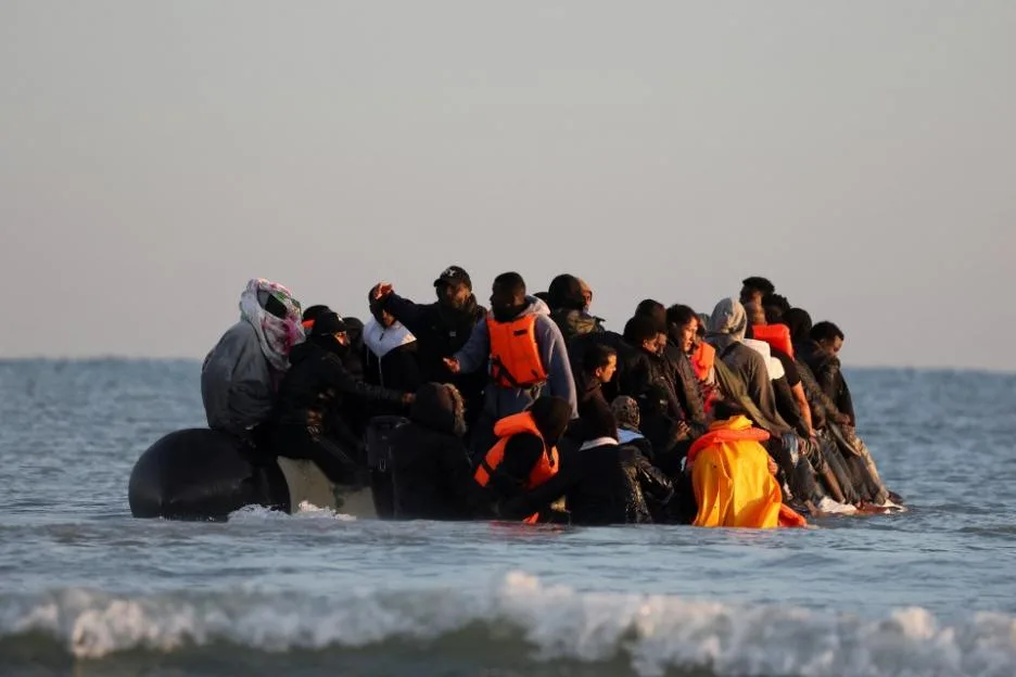 Migrants board an inflatable dinghy in the water, preparing to leave the northern French coast.