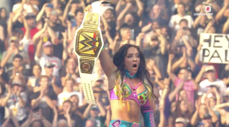 Wrestler Io Shirai holding up a WWE championship belt in a crowded arena.