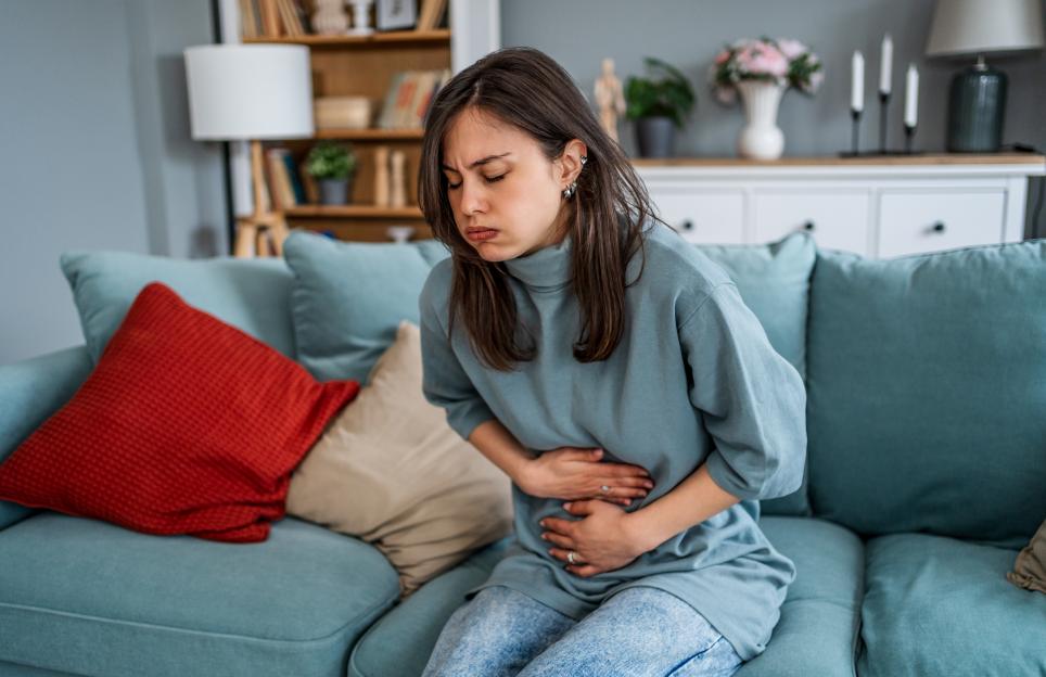 Young woman suffering from a stomach ache while sitting on a sofa.
