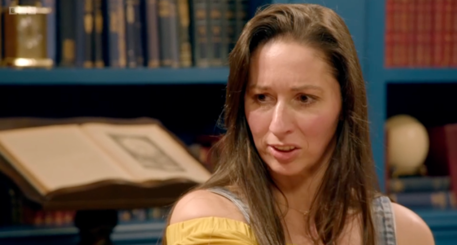 A woman with long brown hair looks concerned or surprised, with bookshelves in the background.