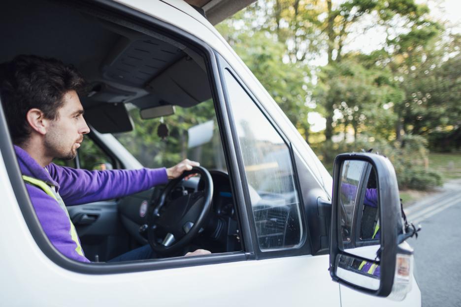 A mid-adult Caucasian delivery man in a purple jacket driving a white semi-truck to deliver bread during the COVID-19 pandemic.