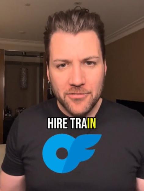 A man with a beard, wearing a black t-shirt with a blue "OF" logo, looks directly at the viewer.