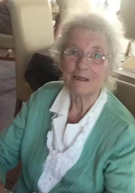 Portrait of Joan Green, a frail elderly widow, wearing a light green cardigan over a white ruffled blouse.