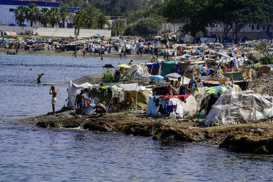 A squalid makeshift refugee camp on the coast of Ceuta, a Spanish enclave, with many migrants on the beach and in the water.