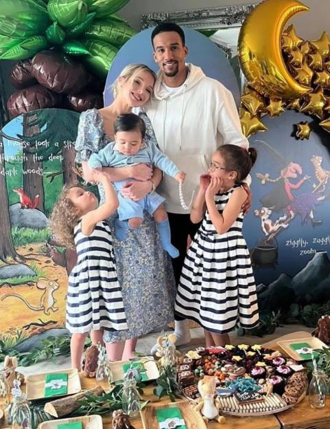 Helen Flanagan, her fiancé Scott Sinclair, and their three children smiling at a party with a decorated table and balloons.