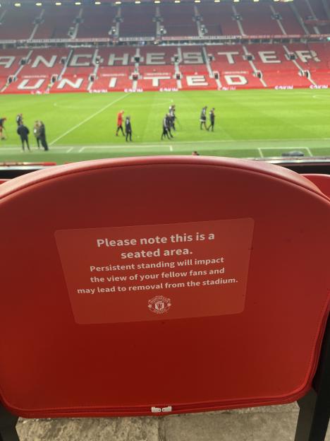 A sticker on the back of a red stadium seat reads, "Please note this is a seated area. Persistent standing will impact the view of your fellow fans and may lead to removal from the stadium."