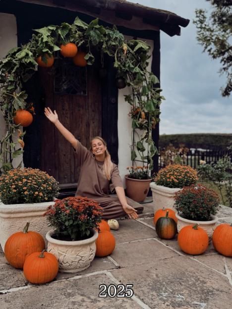 Woman sitting outside house with pumpkins and potted plants for autumn decor.