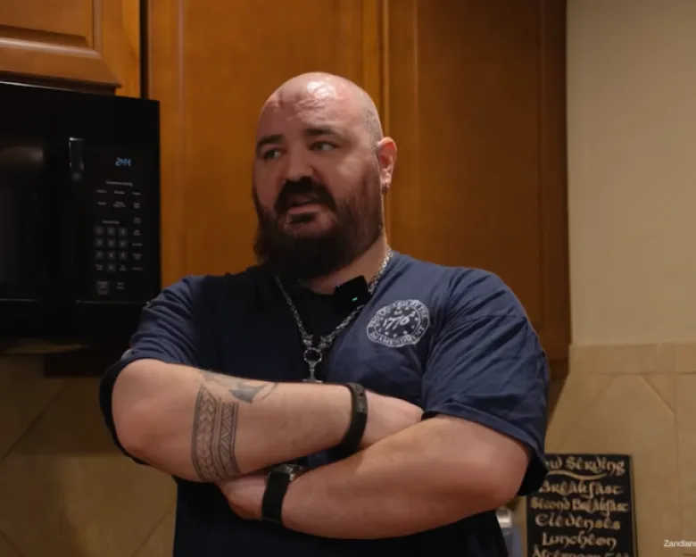 Chris, the husband of a woman in an AI relationship, standing in a kitchen with his arms crossed.
