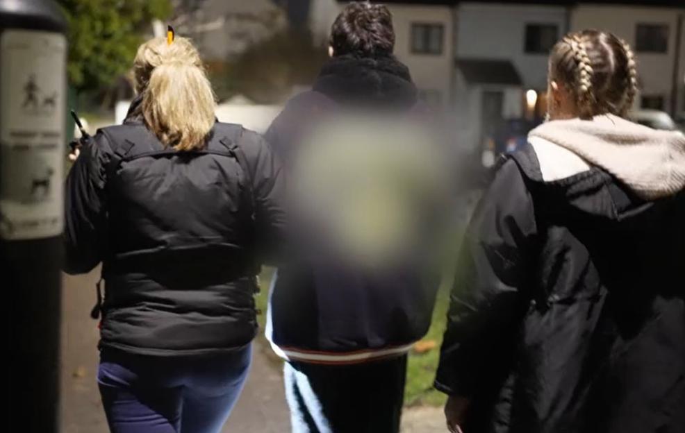 Three people walking away from the camera, with the central person's face blurred out.