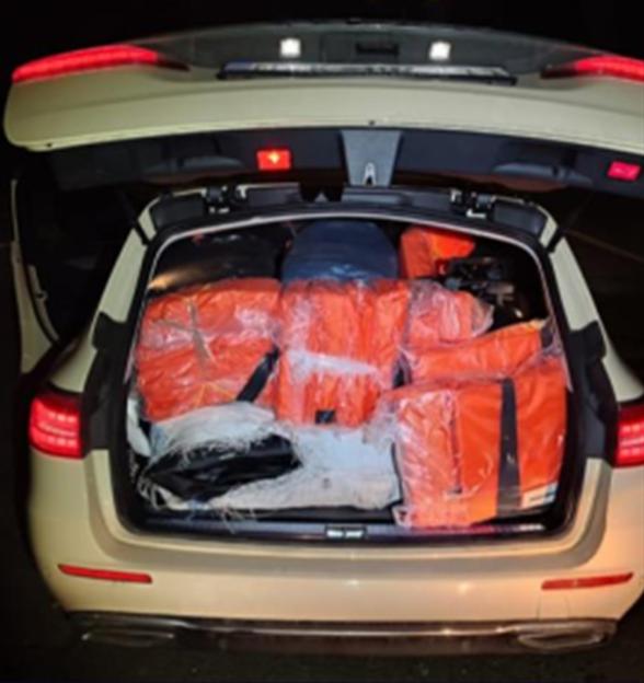 The open trunk of a white car filled with several orange rectangular packages, with some white netting visible in the foreground.