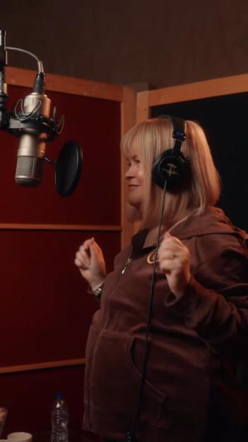 A woman in a recording studio wearing headphones and singing into a microphone.