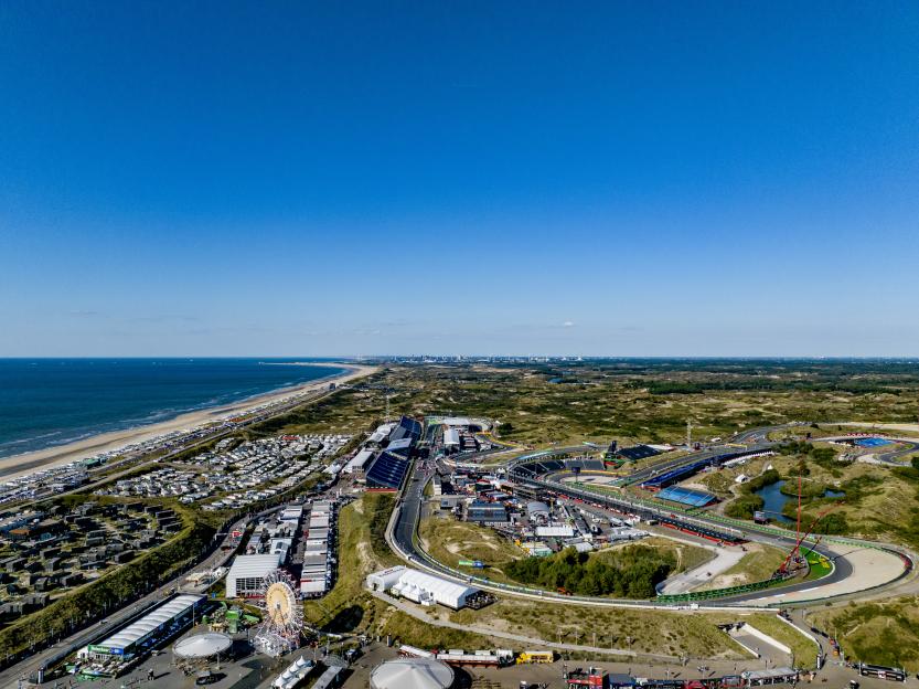 Aerial overview of the Zandvoort Circuit Formula 1 race track, a town with many houses and tents, and the ocean coastline.