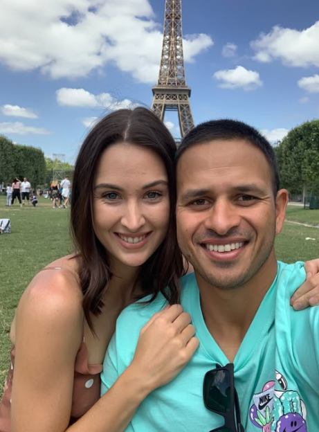 A smiling couple takes a selfie in front of the Eiffel Tower.