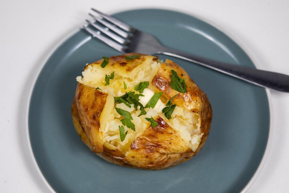 A baked potato with butter and parsley on a blue plate with a fork.