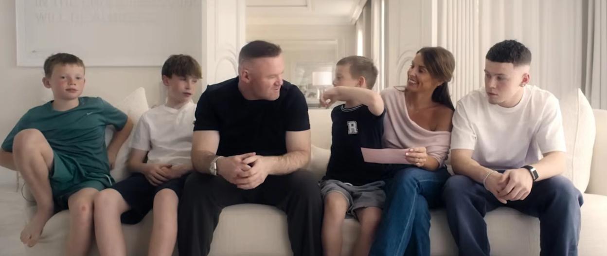 The Rooney family, including Wayne and Coleen, and their four sons, sitting on a sofa in a brightly lit room.
