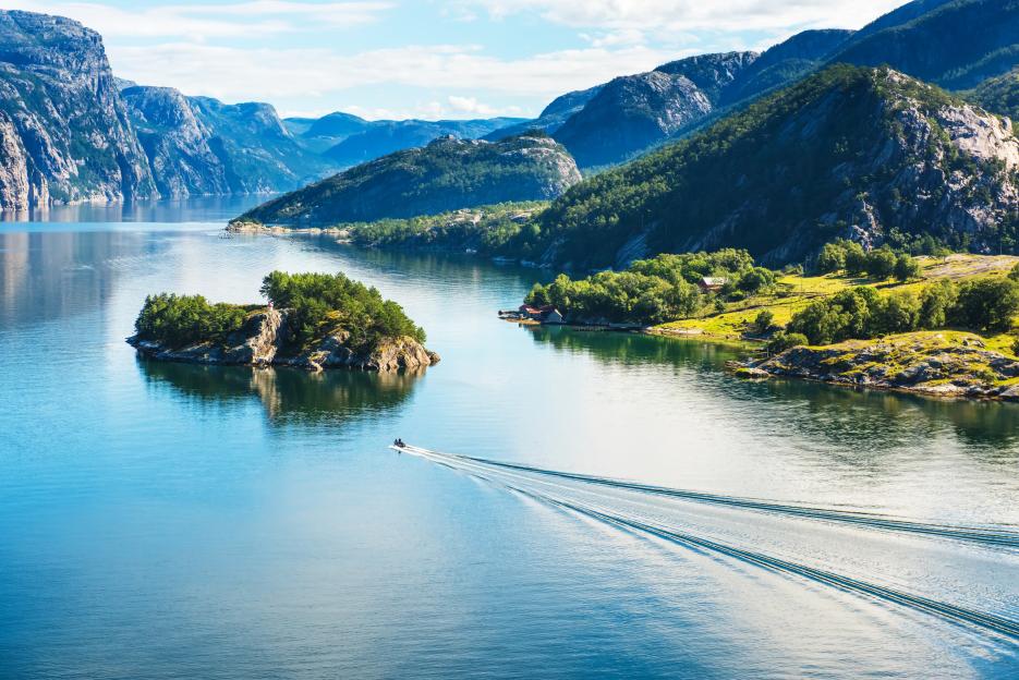 A boat leaving a wake in the Norwegian Lysefjord with mountains in the background.