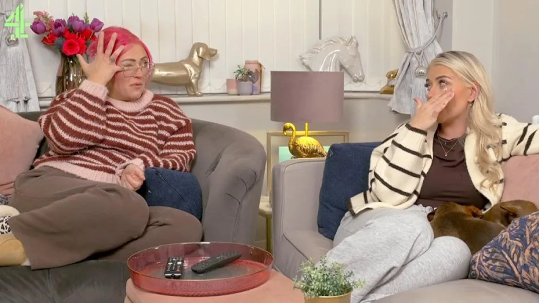 Ellie and Izzi Warner sitting on a sofa, looking emotional and wiping tears from their faces.