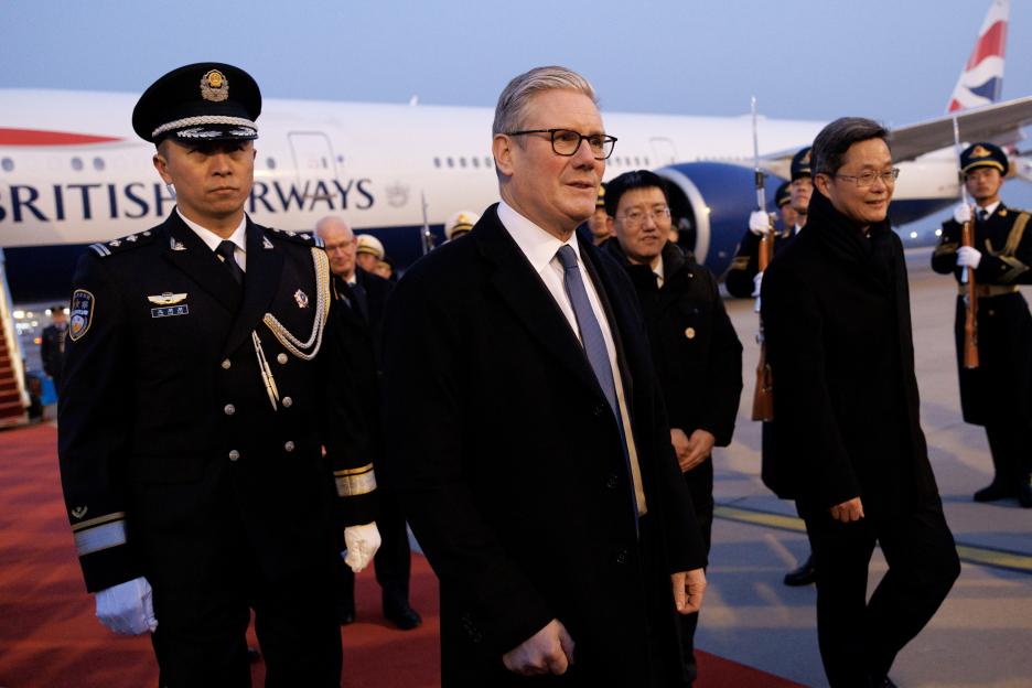 British Prime Minister Keir Starmer walking on a tarmac with officials and guards after arriving in Beijing.