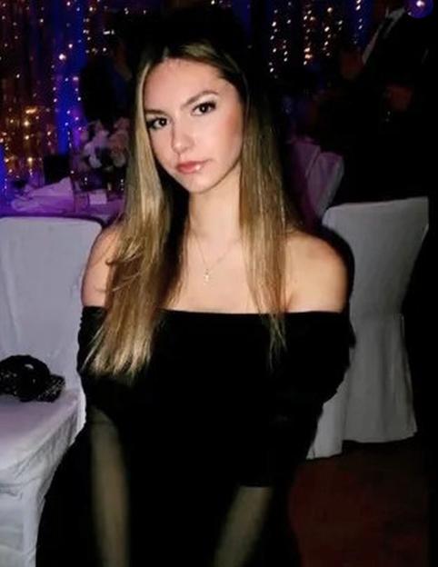 Isabelle Sava, a young woman with long blonde hair, wearing a black off-the-shoulder top and a thin necklace with a small cross pendant.