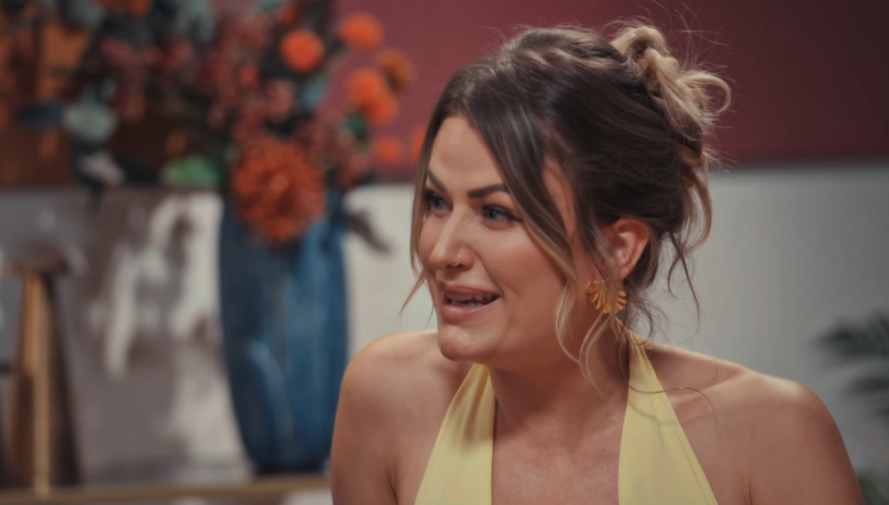 April from MAFS in a yellow dress, with her hair in a messy bun, wearing shell-shaped earrings and a nose ring.