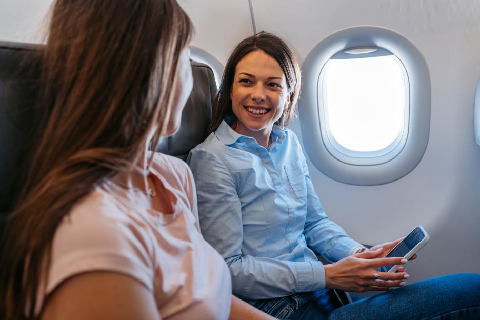 Two Young Female Friends Using Phone And Talking In An Airplane